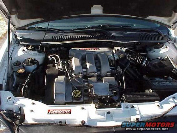 1999 Ford Taurus engine bay with a Flowmaster sticker and Supermotors.net watermark