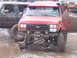 1989 Ford Bronco - A red off-road vehicle with its front passenger-side wheel detached is stuck in the mud.