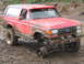 1989 Ford Bronco - Muddy red 1989 Ford Bronco with a detached front wheel, stuck off-road.