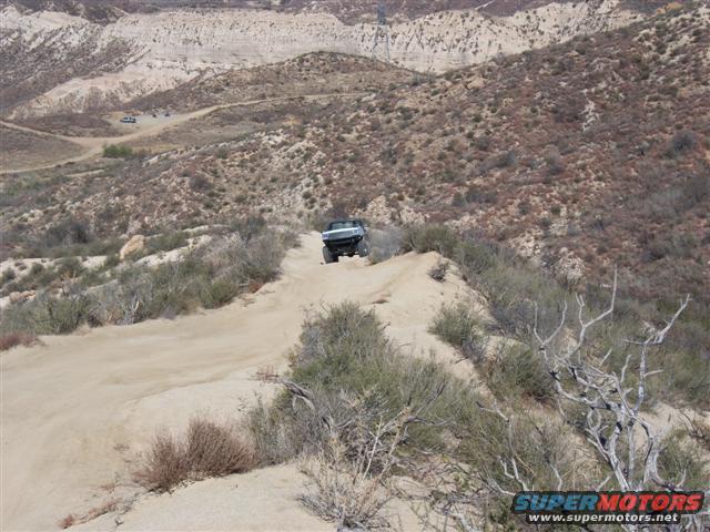 Dark SUV driving on a dirt path in a desert landscape