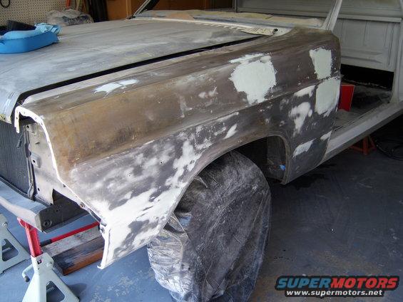 Car body with primer and body filler on fender and hood, sitting on jack stands in a garage