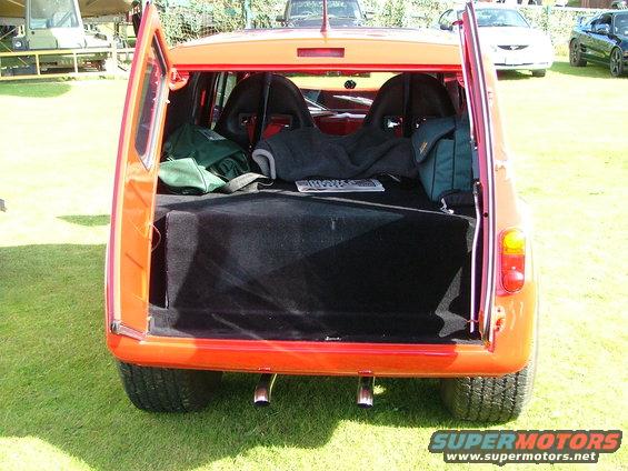 orange hatchback, rear view, open hatch showing racing seats and cargo area, other vehicles in background