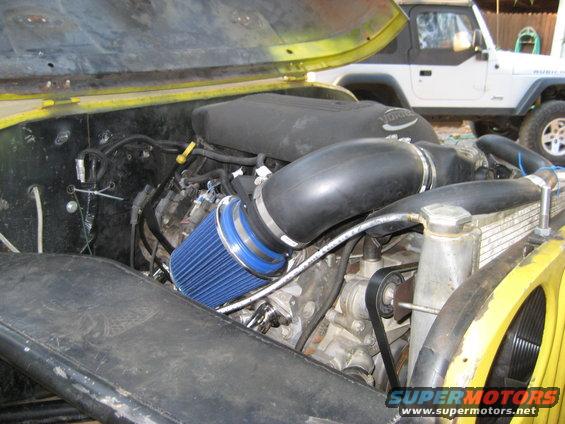 Jeep engine bay with blue air filter and Vortec intake. Another Jeep is parked behind it