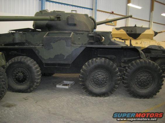 Camouflaged armored car with six wheels and a turret, parked indoors next to another vehicle