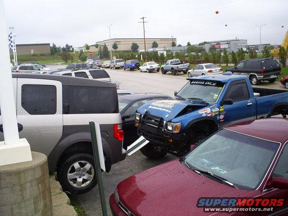 Blue pickup truck with a dented hood and stickers parked in a lot