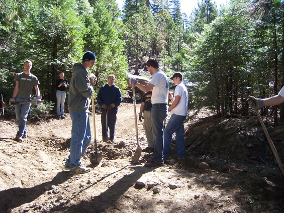 People with shovels and pickaxes working on a dirt path in a wooded area