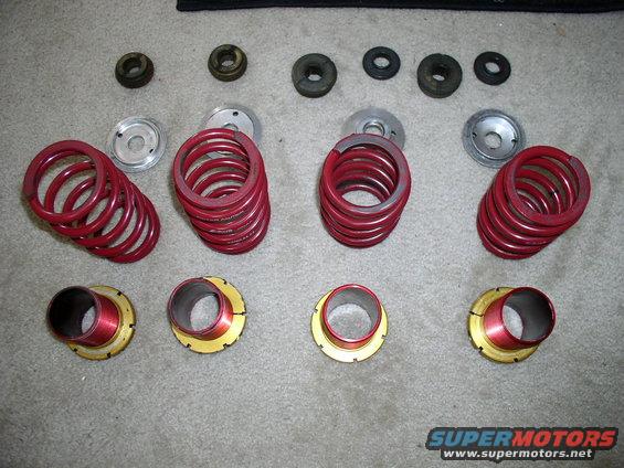 Several red coil springs, metal spring seats, and assorted rubber and metal bushings laid out on a carpeted surface