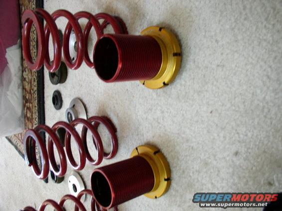 Red coilover suspension parts laid out on a carpeted surface. Some smaller suspension components are also visible