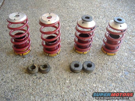 Four red coilover assemblies and four rubber isolators on a concrete surface