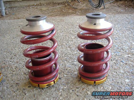 Two red coilover suspension springs with silver and gold adjusters on a concrete surface