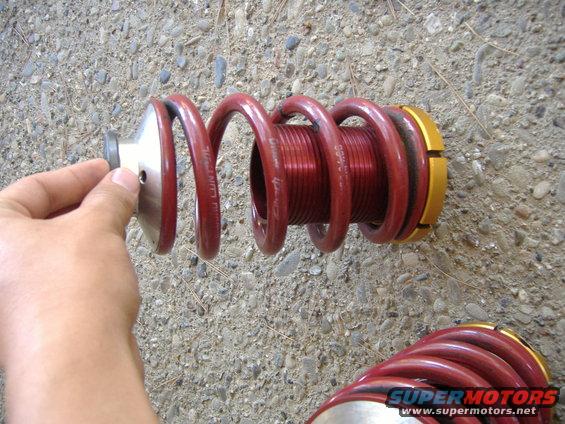 Red coilover suspension part with gold adjustment collars held by a hand