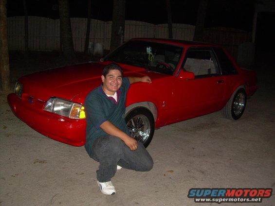 Red 1990s Ford Mustang coupe with chrome wheels. Man crouching beside it