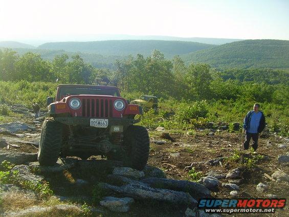 Red 2003 Jeep Wrangler on rocks with a man and another jeep in background