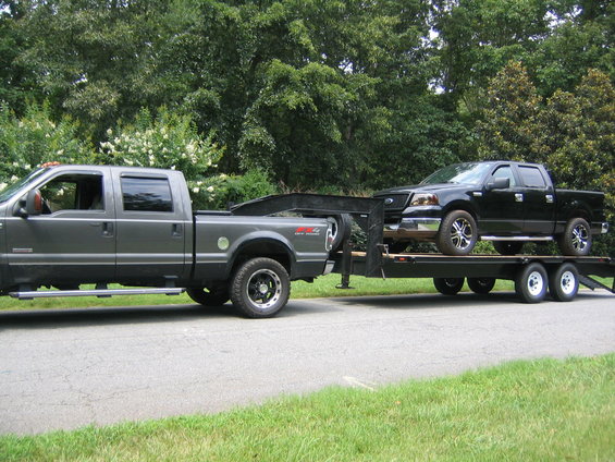 Black Ford F-150 on trailer, towed by grey Ford F-250