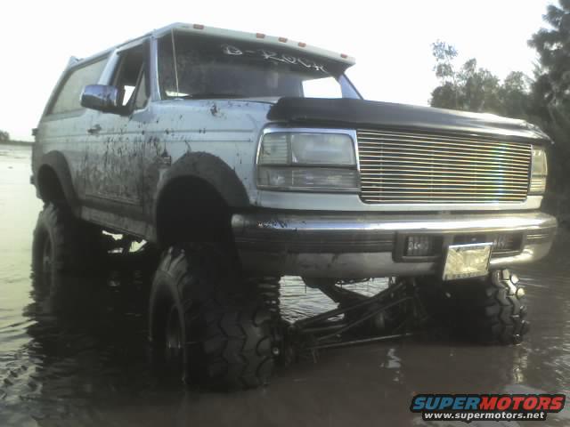 Lifted 1995 Ford Bronco covered in mud, driving through shallow water