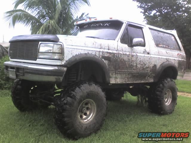 Mud-covered lifted Ford Bronco with large tires parked on grass