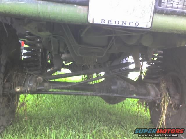 Underside of a green Ford Bronco, showing suspension and drivetrain components covered in grass and mud