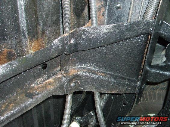 Underside of a vehicle showing frame rails, suspension components, and some rust