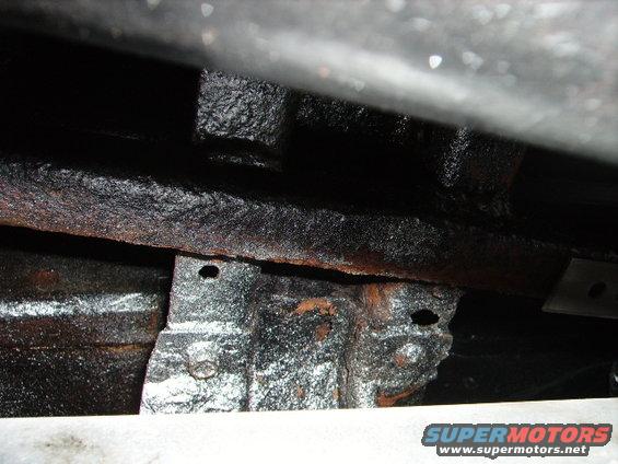 Undercarriage frame with rust and black undercoating. Visible bolts and mounting brackets