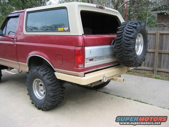 Red Ford Bronco with tan top, spare tire mounted on rear, aftermarket bumper