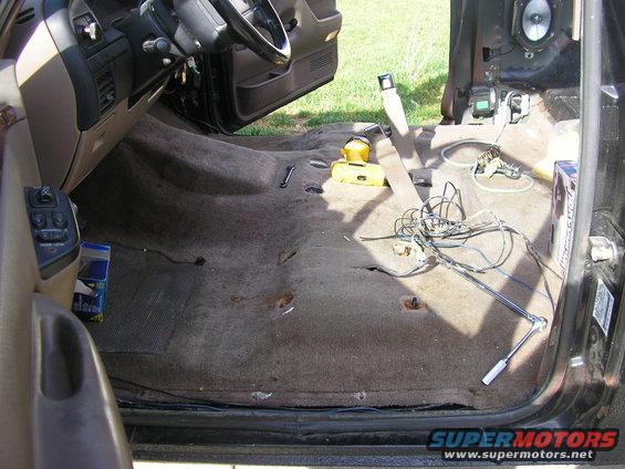 Interior of a vehicle with carpet removed, showing wiring and tools on the floor