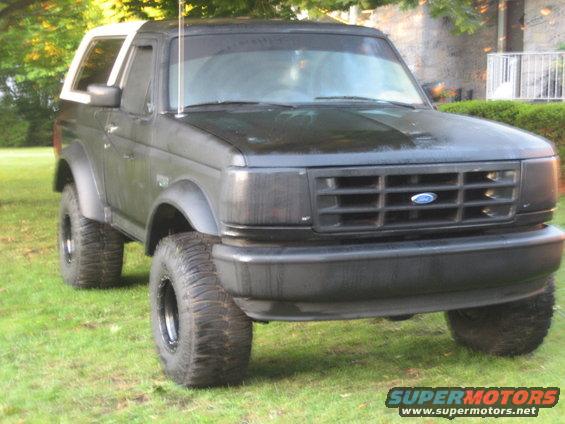 Black Ford Bronco with white removable top, lifted suspension, and off-road tires parked on grass