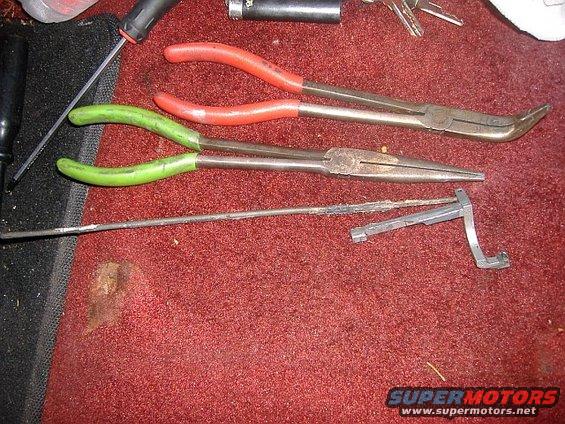 Several long-nosed pliers and a screwdriver on red carpet. A metal clip is also visible