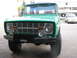 1975 Ford Bronco - A green 1975 Ford Bronco is parked outside a building, with another vehicle visible in the background.