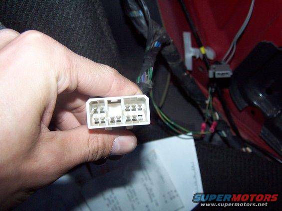 Hand holding a white wiring harness connector with multiple pins