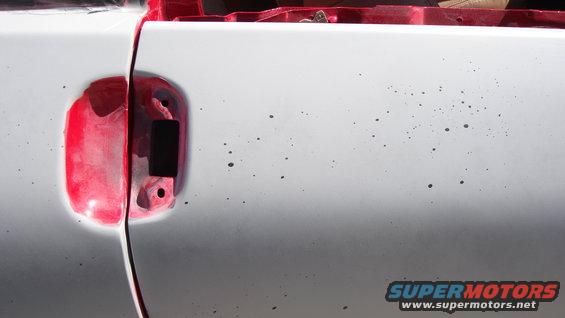 White car door with red fuel filler door removed, showing primer and black interior