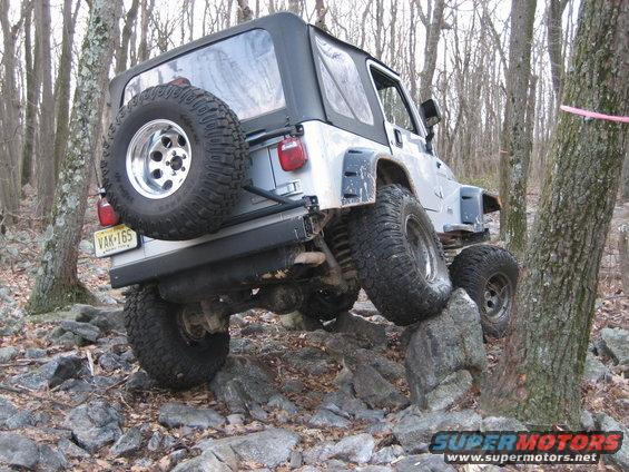 Silver Jeep Wrangler with spare tire on rear, driving over rocks