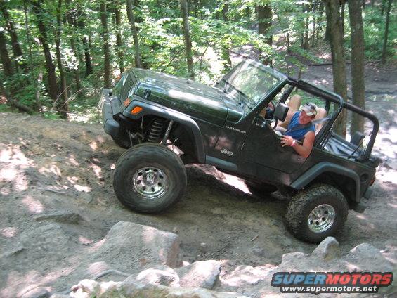 Green Jeep Wrangler TJ model navigating a rocky trail with a driver visible
