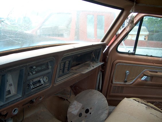 Interior of an old truck, dashboard and door panel visible. Another vehicle is seen through the windshield