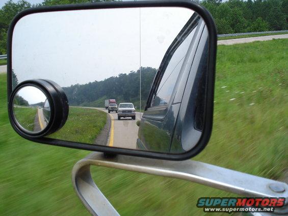 view in side mirror shows a white pickup truck and a semi-truck on a highway