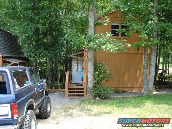 Dark blue SUV with large tires parked on gravel near a wooden cabin