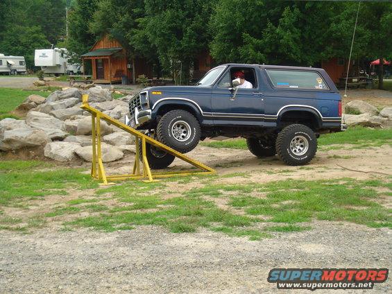 Blue Ford Bronco with lifted suspension driving over a yellow obstacle