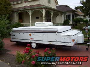 Pop-up camper trailer parked in driveway, house in background