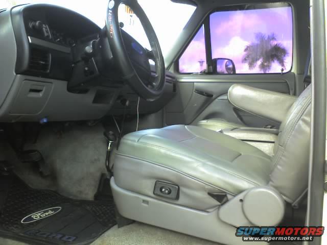 Interior shot of a truck, showing gray leather seats, dashboard, and steering wheel. Ford logo on floor mat