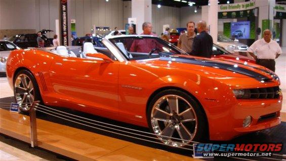 Orange convertible sports car with black racing stripes and chrome wheels on display
