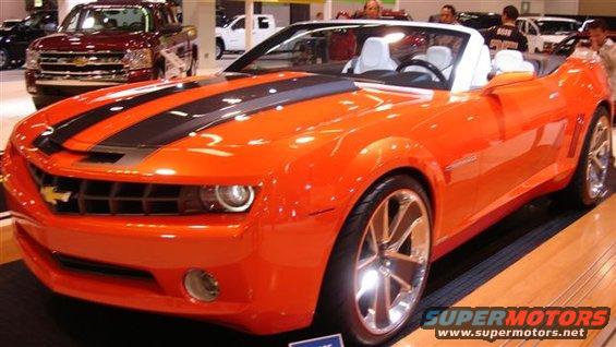 Orange convertible sports car with black racing stripes on display, red pickup truck in background