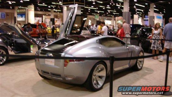 Silver concept car with gullwing doors open, rear view, at an auto show