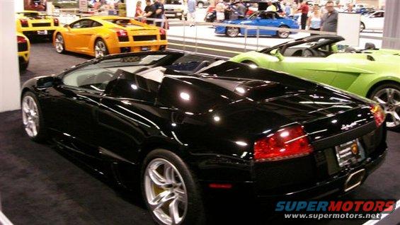 Black convertible sports car with yellow brake calipers, parked indoors with other cars