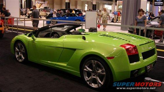Lime green convertible sports car with black top, seen from the rear-right at an auto show