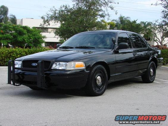 Black Ford Crown Victoria police car with a push bumper, parked on asphalt