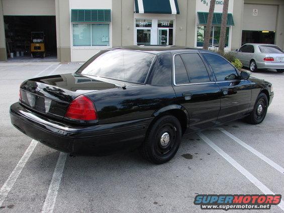 1998 Ford Crown Victoria parked on asphalt, rear quarter view. Another silver sedan is parked in the background
