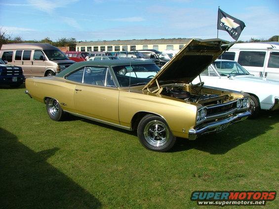 gold coupe with green roof, hood open, parked on grass with other vehicles