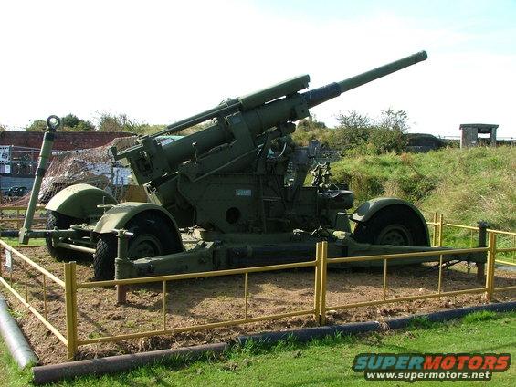 Green anti-aircraft gun on a trailer, viewed from the front-right, behind a yellow barrier
