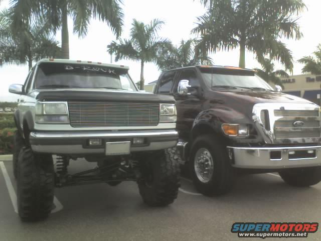 Lifted white truck with chrome grille next to a lifted dark red truck with chrome grille