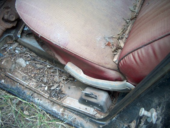 Interior of a 1979 Ford Bronco showing a worn red seat and debris on the floor