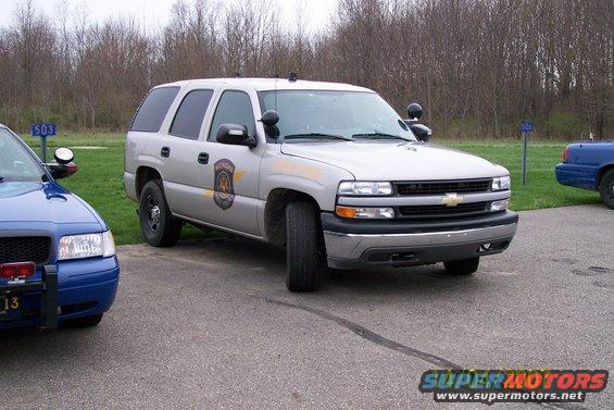 Silver Chevrolet Tahoe with police markings parked next to a blue police car